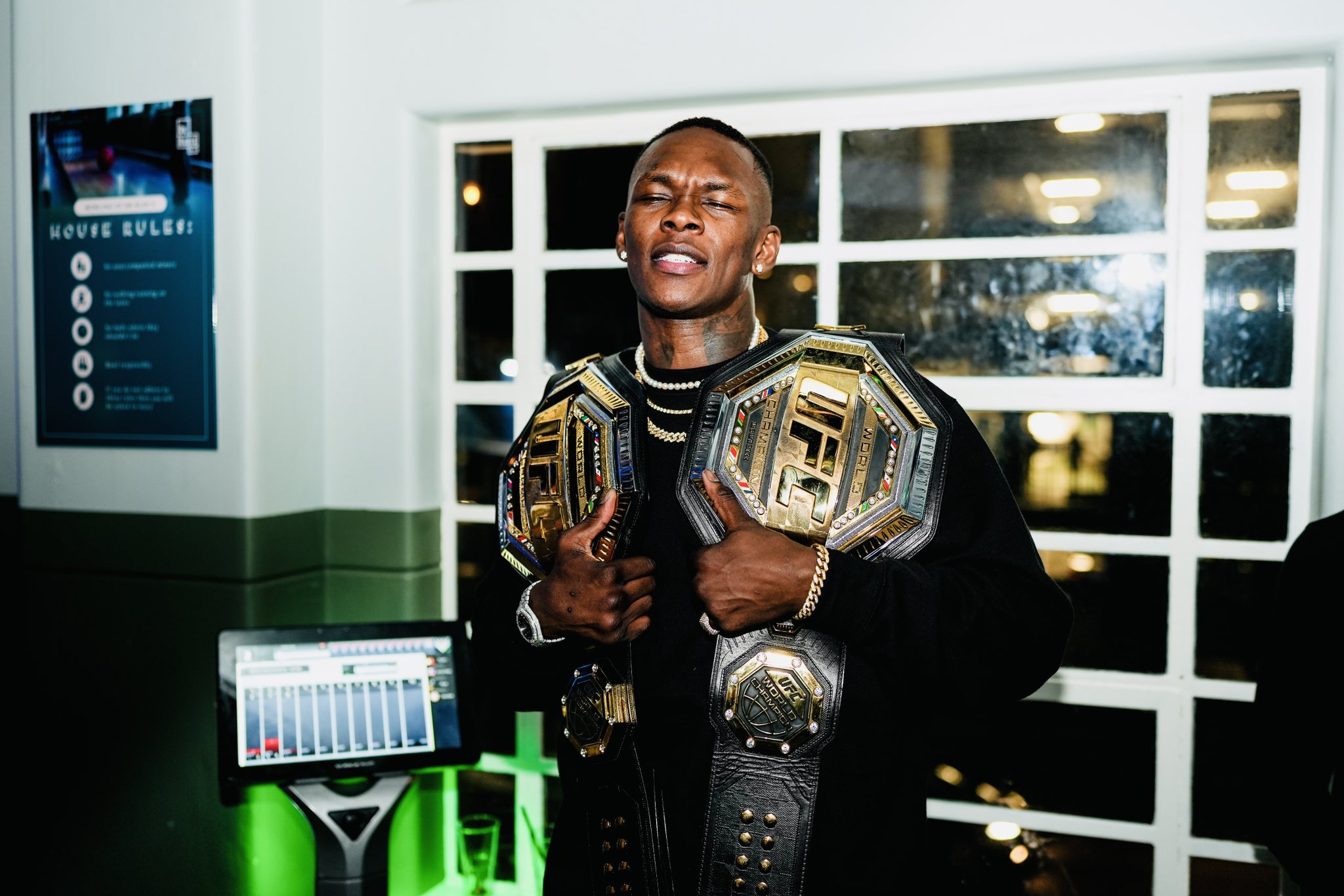 Israel Adesanya posing with his belts
